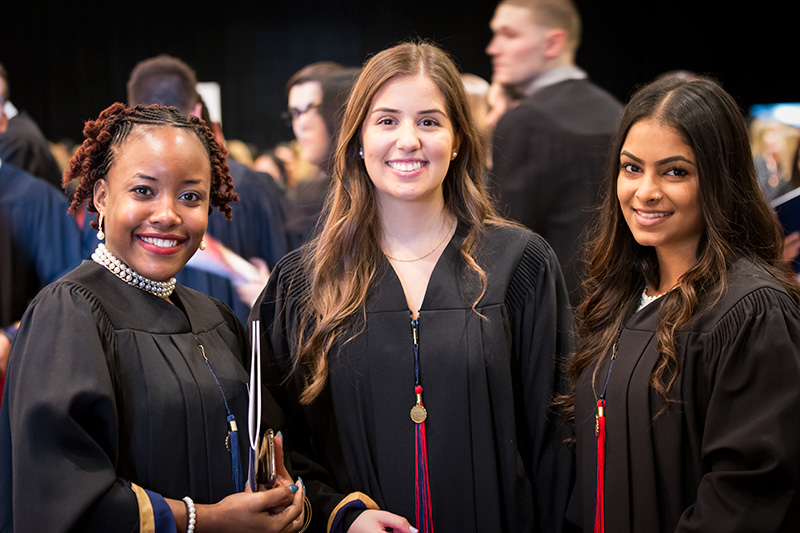 Three students in graduation gowns smiling