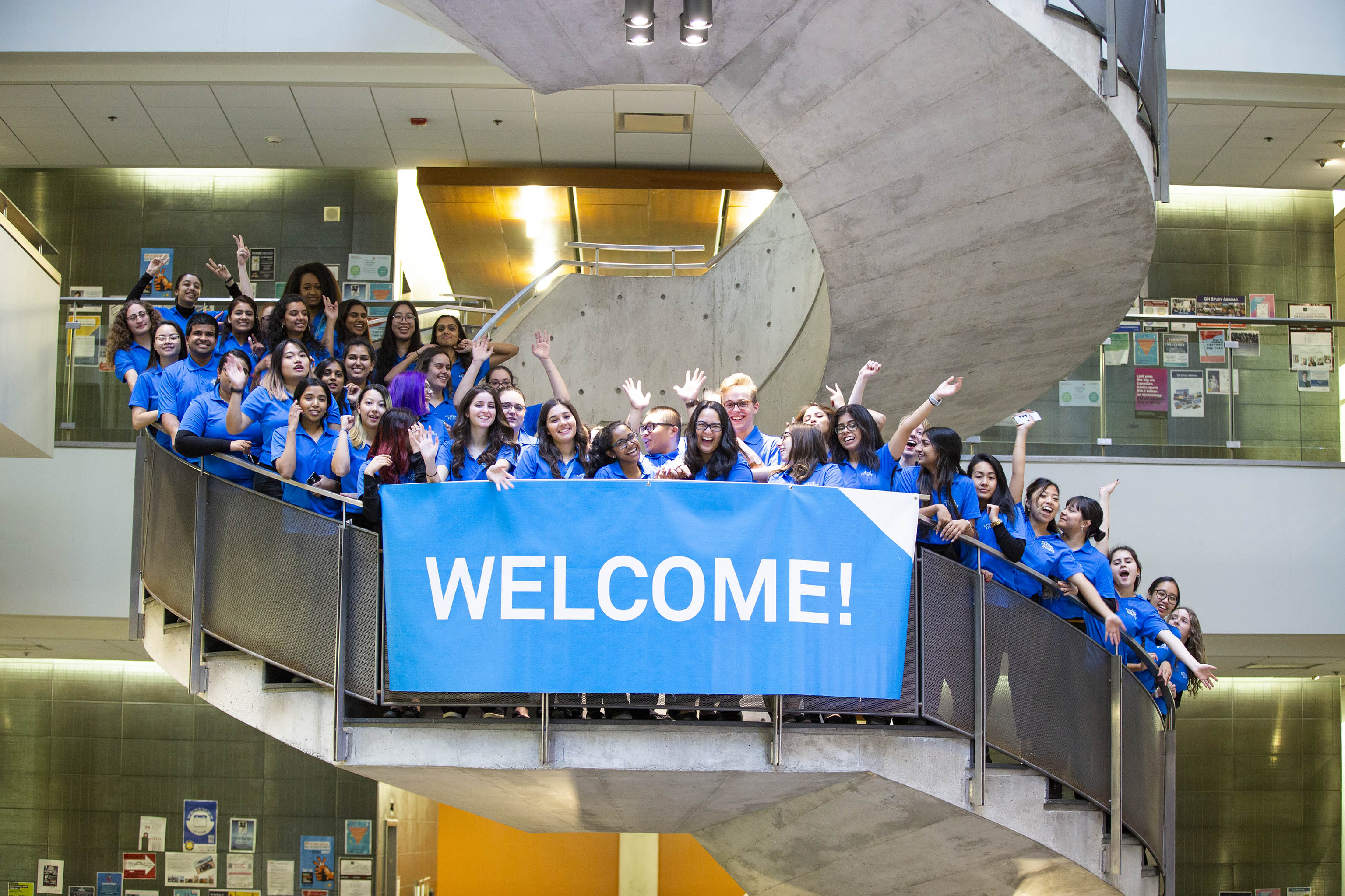 A group of students standing on a staircase with a sign saying Welcome
