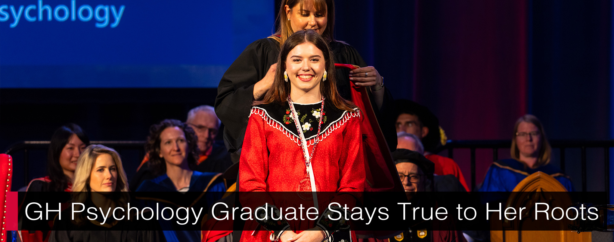 Kristen Brant in traditional Indigenous clothing smiling while waiting for someone to put the University of Guelph-Humber convocation hood over her. There are people in convocation regalia sitting behind, watching. Text reads, 