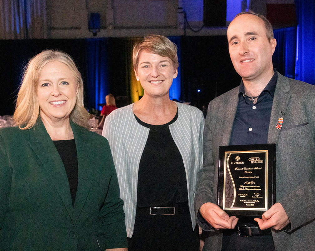 Three individuals posing for a photo where one is holding an award