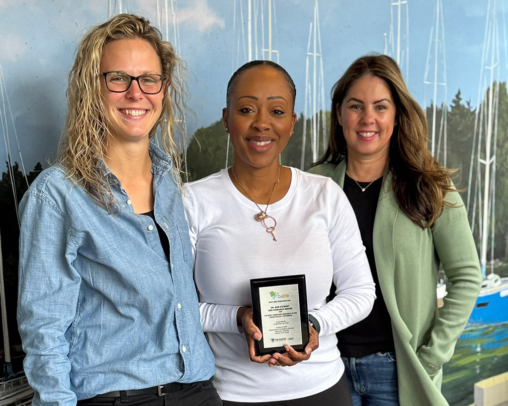 Three individuals standing next to each other while the middle person is holding an award