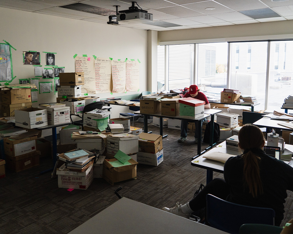 A room full of boxes and papers taped to wall with two students working in it