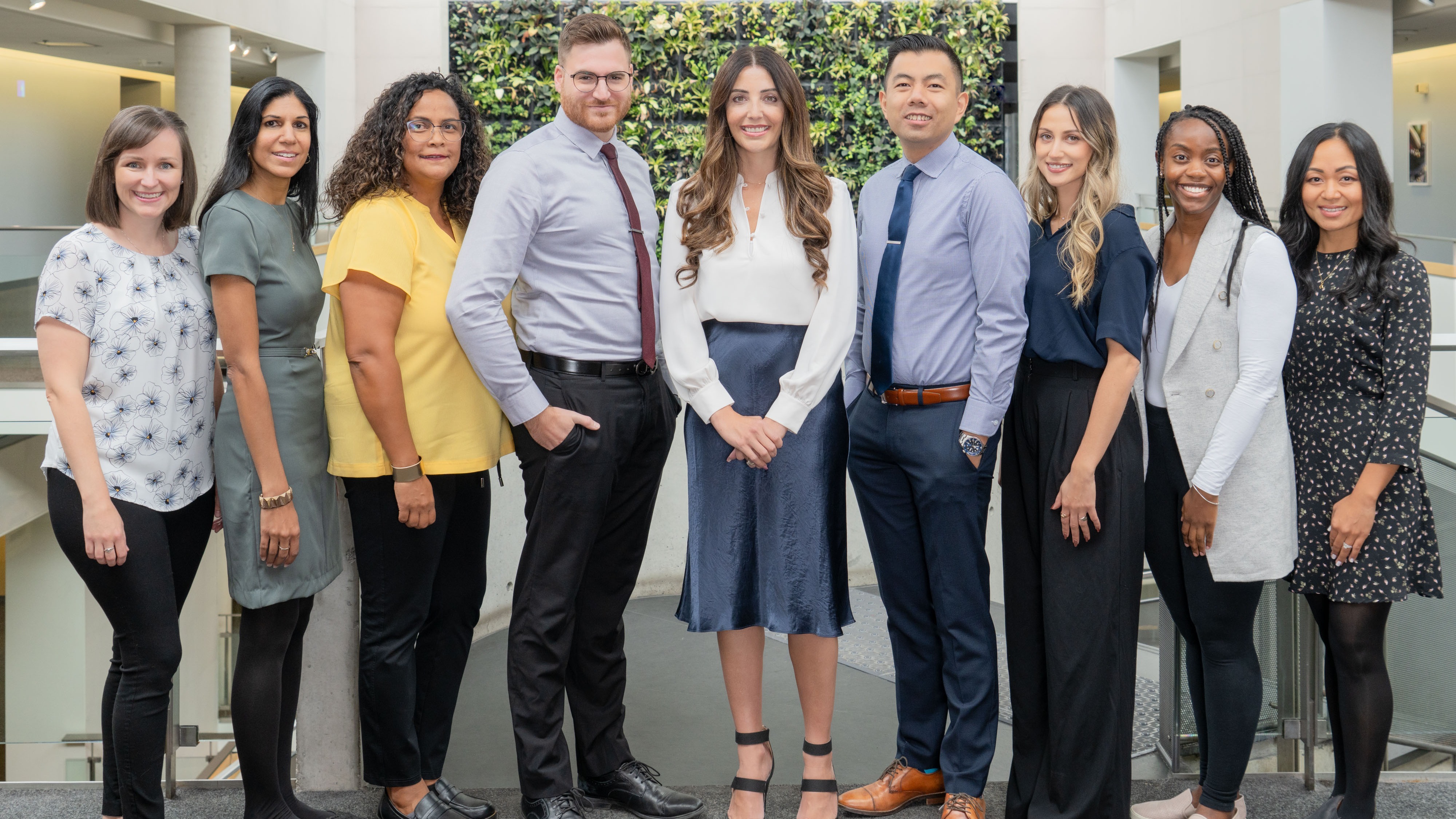 A group of nine academic advisors posing with the plant wall in the background
