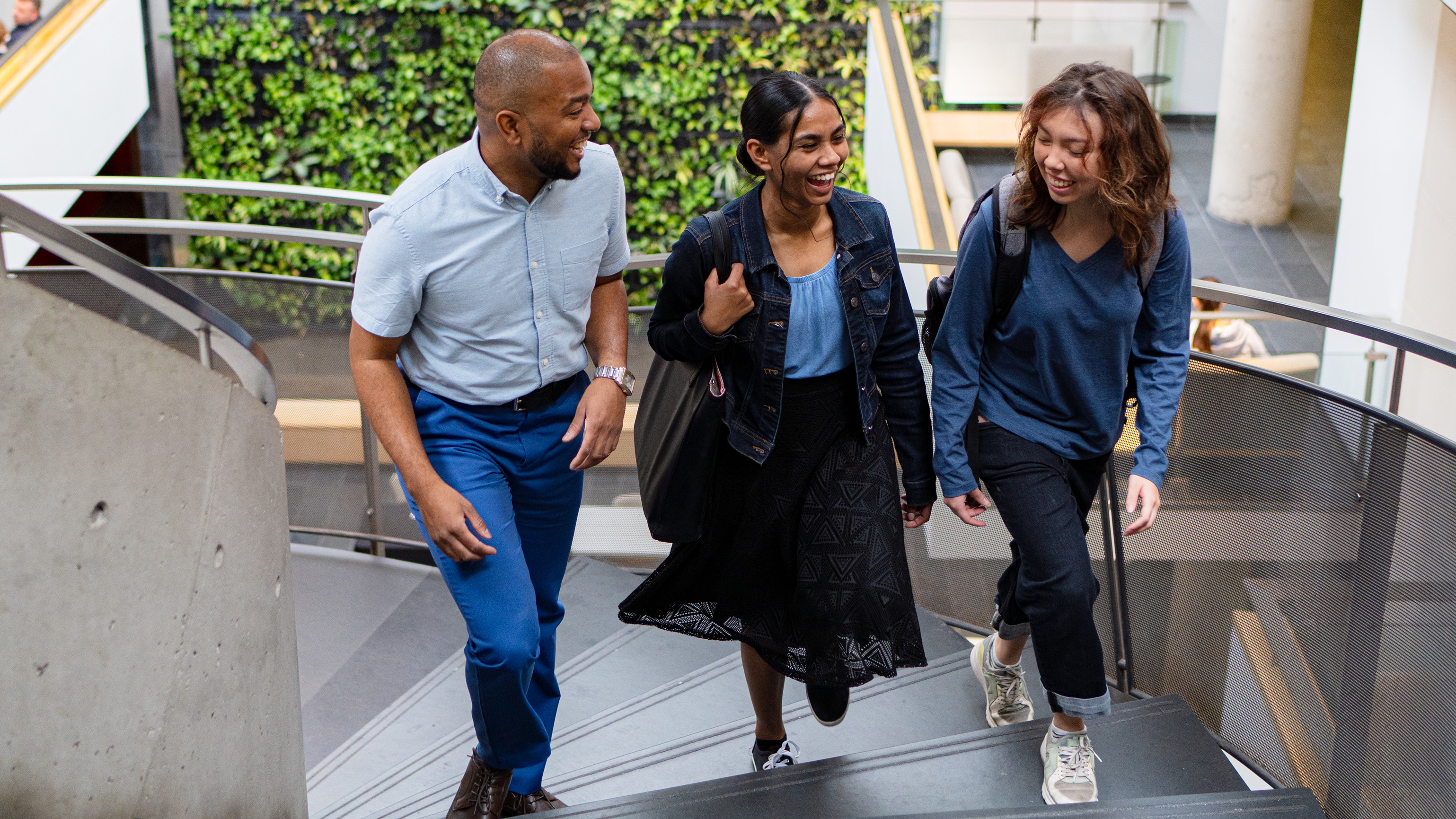 Three students walking up the stairs with plant wall in background