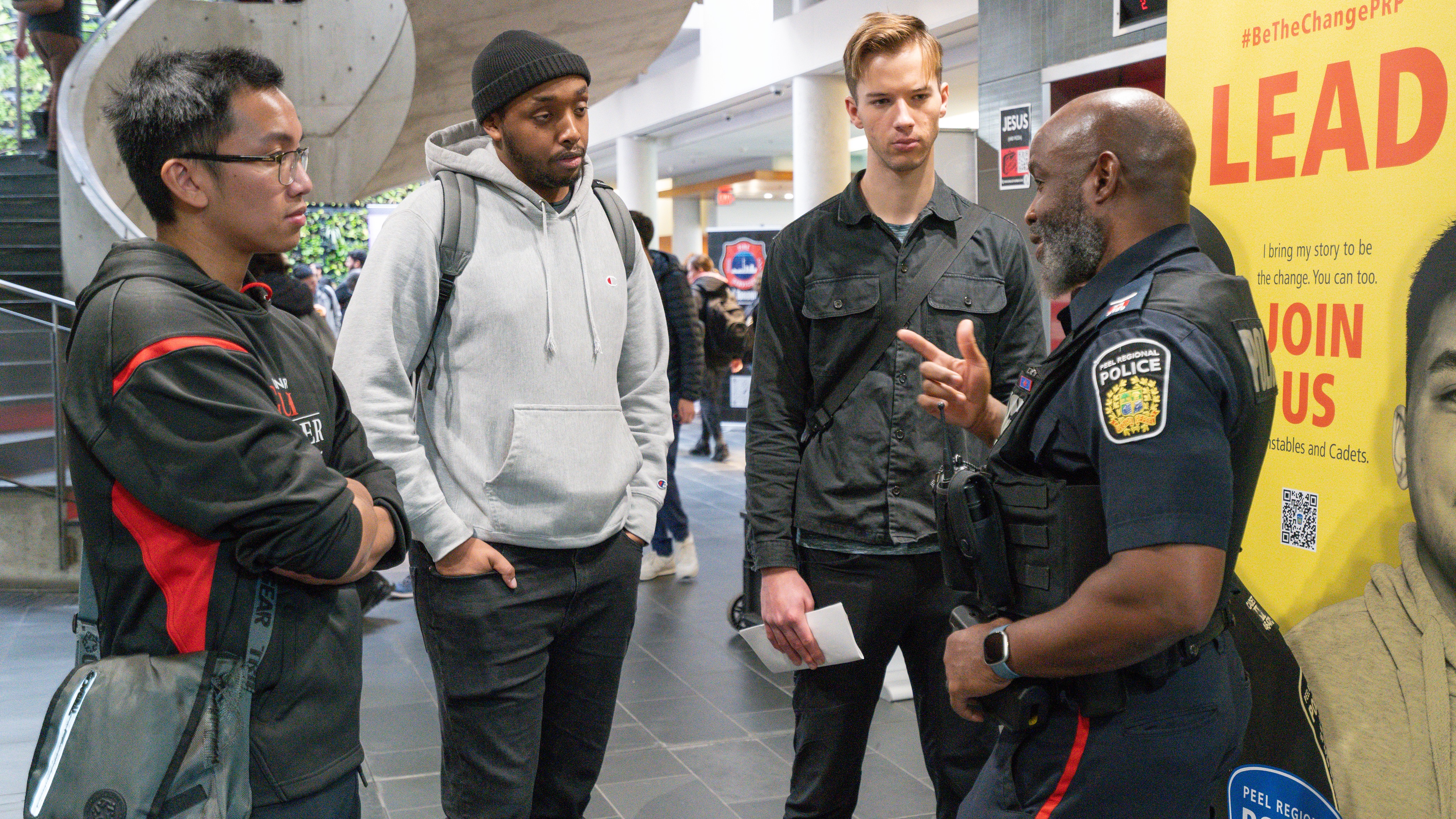 Three students standing speaking with a police officer at a career fair