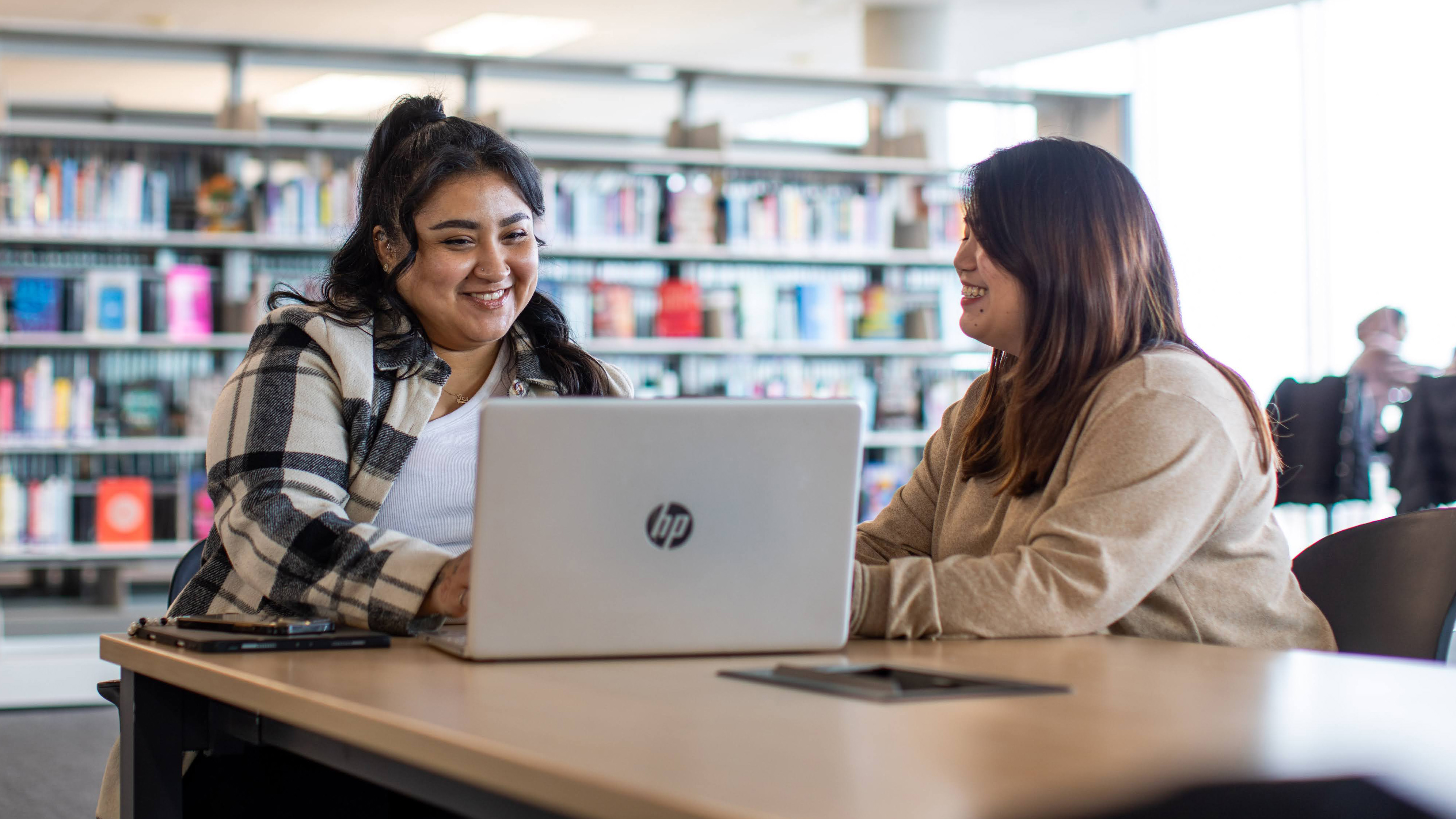 Two women in front of a laptop with library stacks in the background