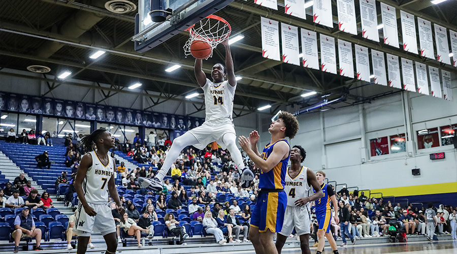 A student-athlete doing a slam dunk while two teammates and an opponent watch on
