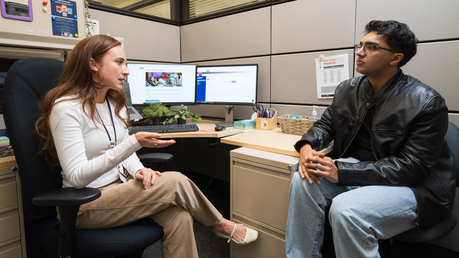 An advisor speaking to a student in their cubical office.