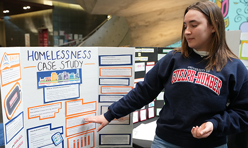 SSWS case study Female student with U of GH sweater in front of poster