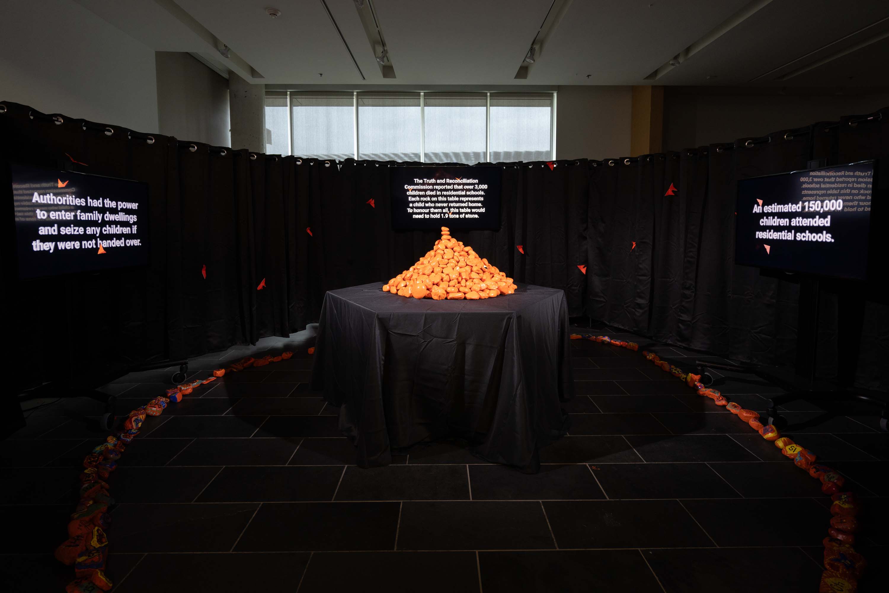 Echos in orange art exhibit with black curtains and pile or orange stones