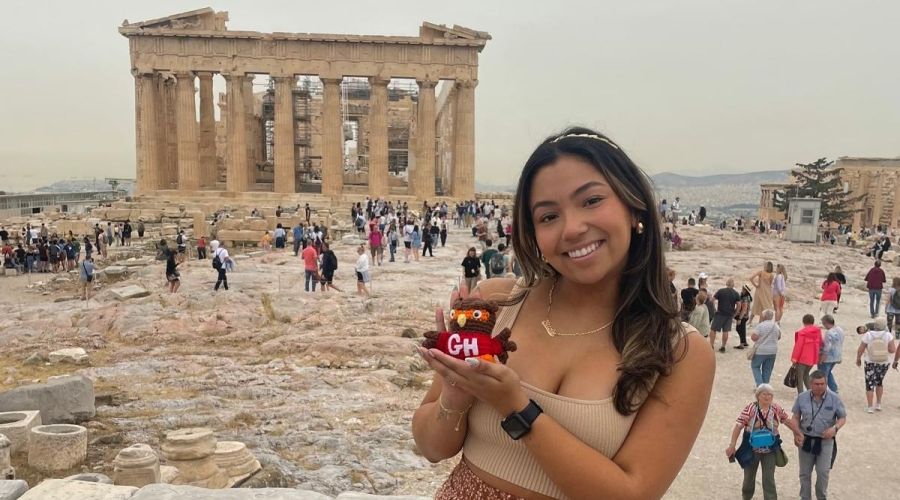 Woman holding mini Swoop figurine in front of Greek ruin